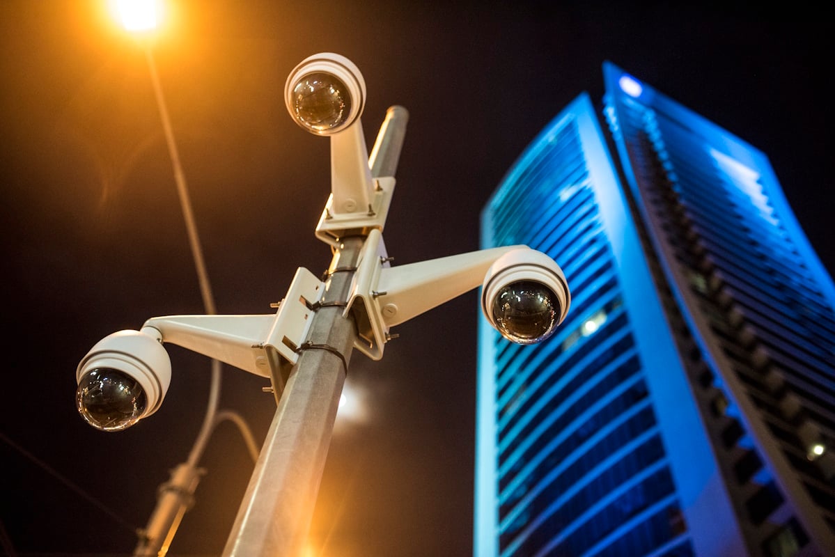 Cluster of modern dome security cameras mounted on a pole in an urban setting at night, with a tall illuminated building and streetlight in the background.